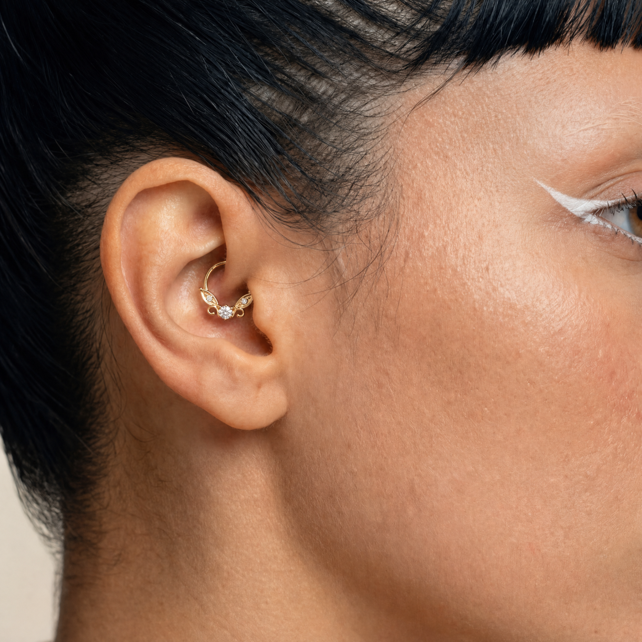 Anneau piercing Celia porté au daith en titane gold avec zircon central serti, petits zircons latéraux et détails en forme d’ailes