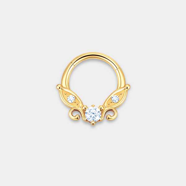 Anneau piercing Celia en titane gold avec zircon central serti, petits zircons latéraux et détails en forme d’ailes de face