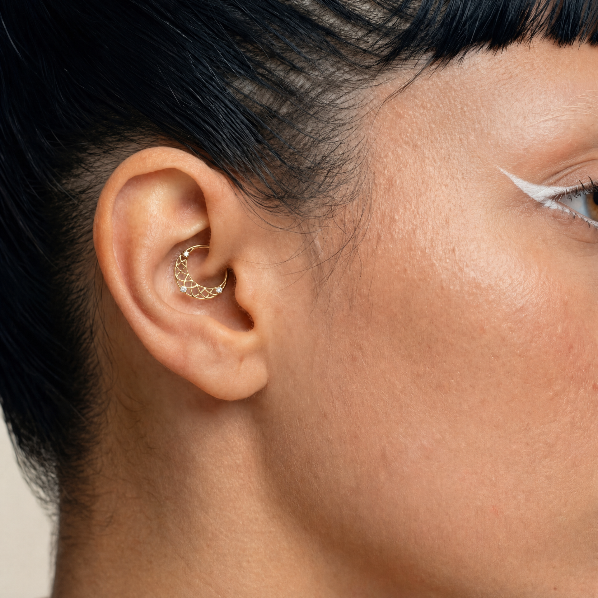 Anneau piercing Lumis porté au daith en titane gold avec motifs géométriques ajourés et trois zircons sertis