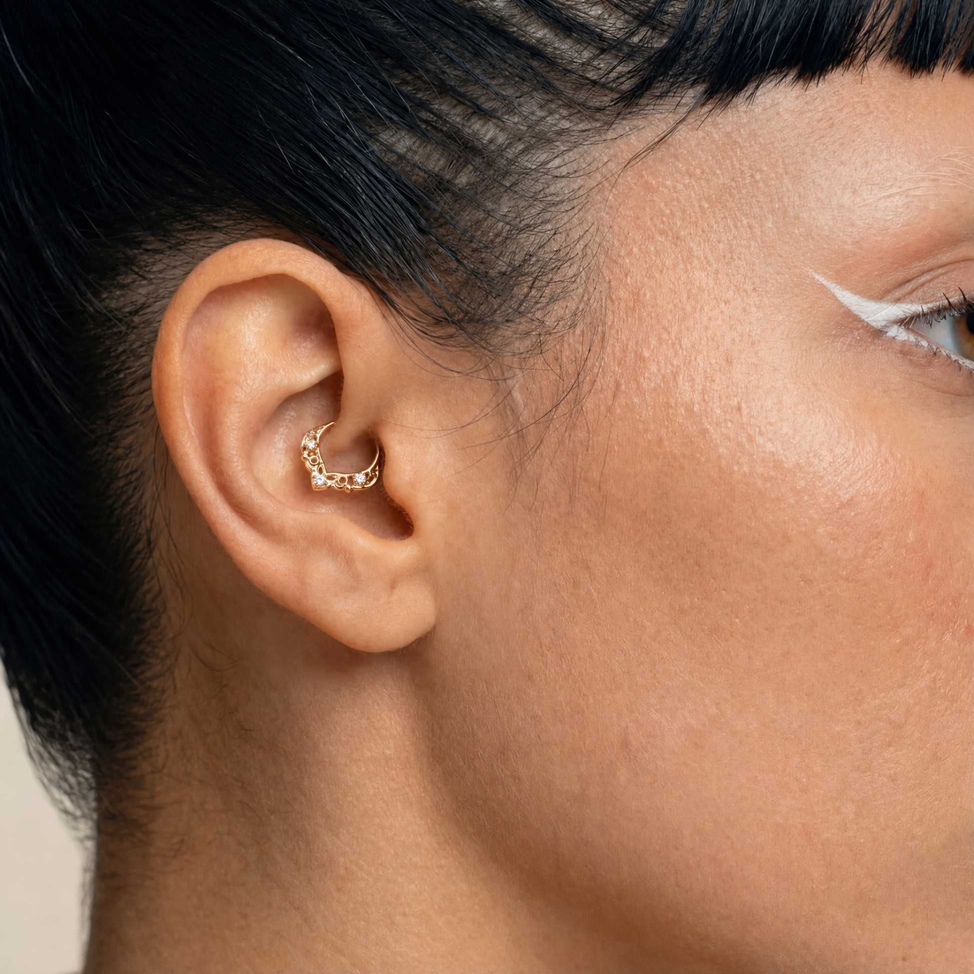Anneau piercing Orion porté au daith en titane gold avec détails ajourés délicats et trois zircons sertis
