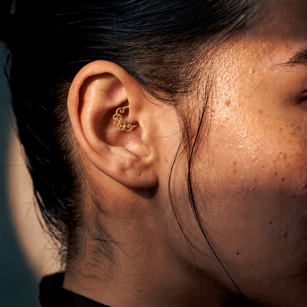 Anneau piercing Spira en titane gold, motif de volutes entrelacées, porté au daith