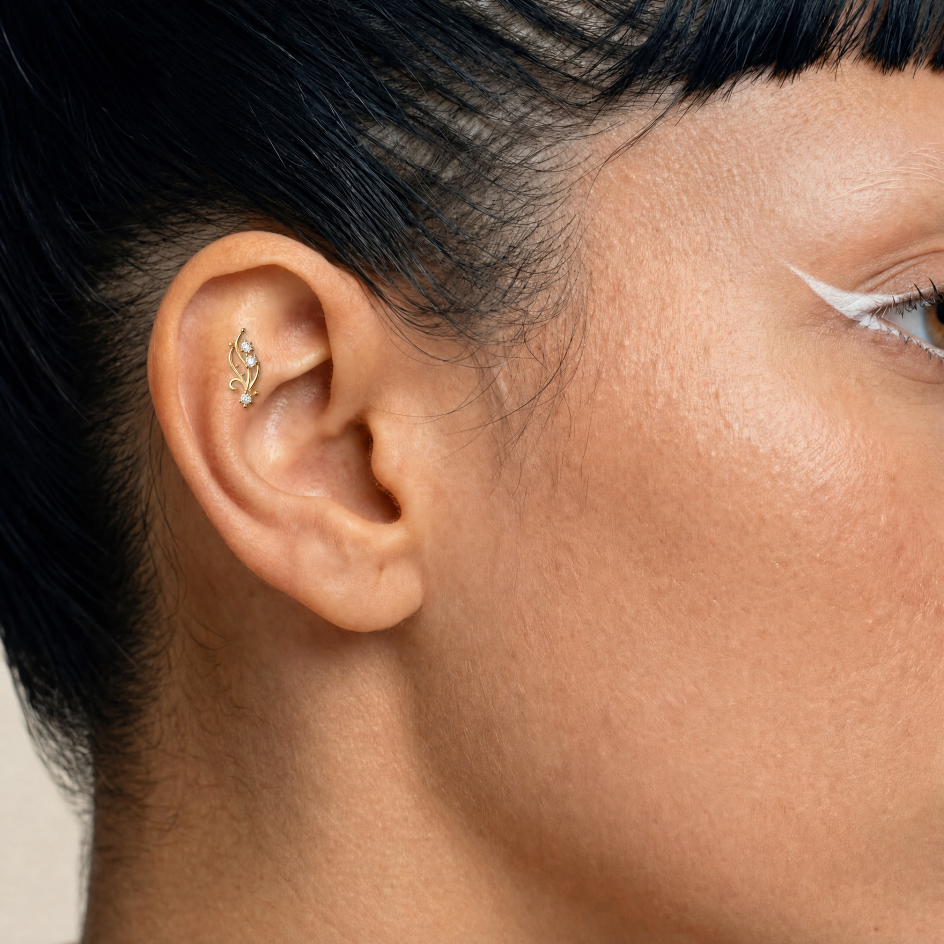 Embout piercing Brina porté au flat en titane gold avec trois zircons sertis et courbes délicates inspirées de motifs végétaux